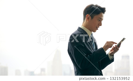 A male business person using a smartphone with a city in the background A male business person using a smartphone with a city in the background 132153952