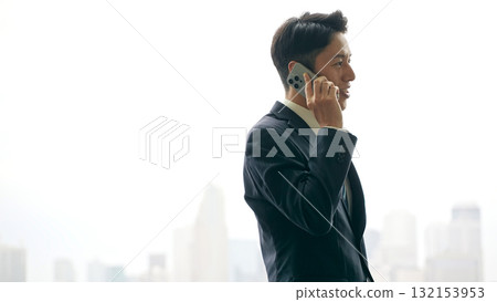 A male business person talking on a smartphone with a city in the background A male business person talking on a smartphone with a city in the background 132153953