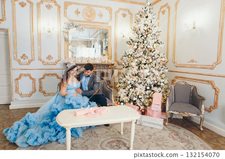 married couple sitting together. husband put his hand on his pregnant wife's belly. pregnant girl in a lush blue dress. young man in a blue shirt. family photo session.  132154070