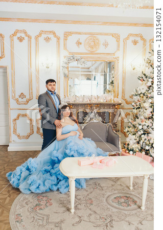 a husband in a suit stands behind his pregnant wife. put his hand on the shoulders of his pregnant wife. pregnant girl in a lush blue dress. young man in a blue shirt. portrait photography. family 132154071