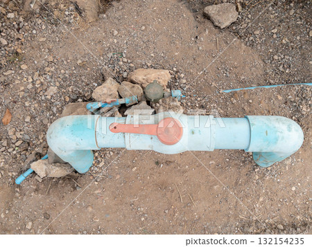 Red Plastic Water Valve on PVC Pipe in Rural Area. 132154235