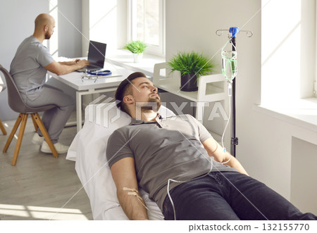 Young male patient getting vitamin or medication solution through IV line at clinic 132155770