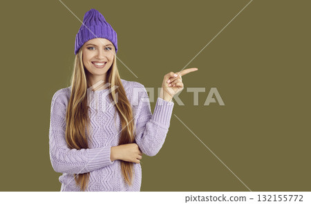 Beautiful woman in warm outfit presents copy space pointing to side with her index finger. 132155772