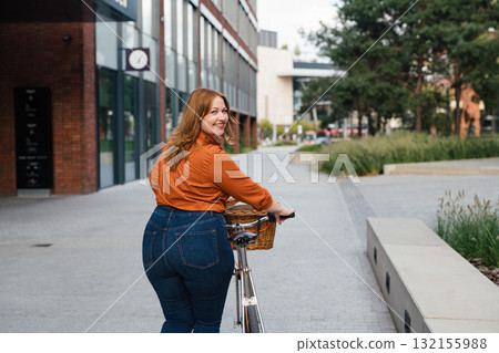 Female city commuter walking with bike to office. 132155988