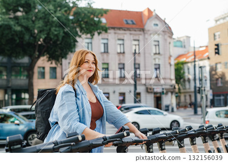Curvy woman unlocking shared e-scooter in city. 132156039