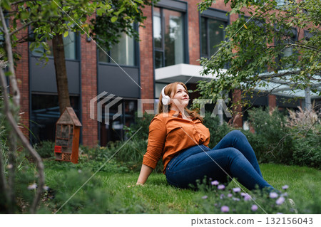 Confident woman relaxing, listening podcast outdoors in park. 132156043