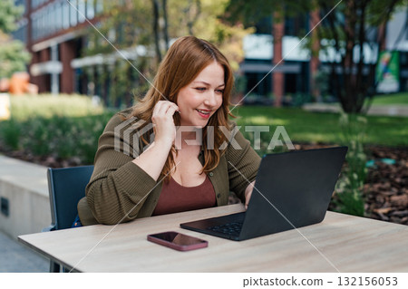 Plus size woman working on laptop outdoors. Plus size woman working on laptop outdoors. 132156053