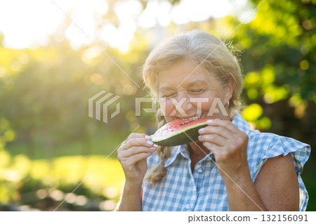 Lovely senior woman eating slice of watermelon in garden. Lovely senior woman eating slice of watermelon in garden. 132156091