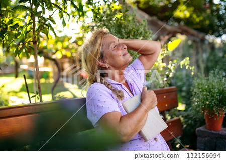 Selfacare moment for elderly woman, quiet reading time in garden. 132156094