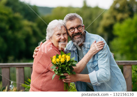 Portrait of mature son bringing bringing flowers to old mother. 132156130
