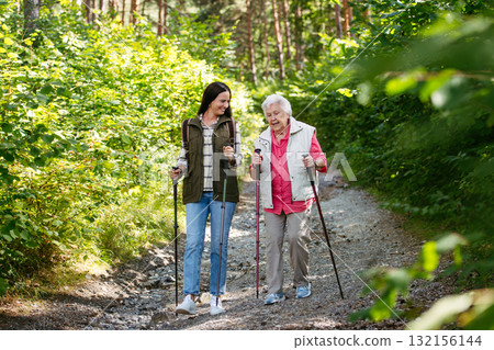 Senior woman and daughter enjoying hike with trekking poles. 132156144