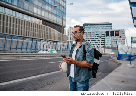 Mature man walking home from work, texting on smartphone. 132156152