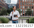Businessman in front of office building, holding tablet and reading something. 132156157