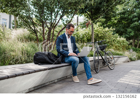 Manager working in urban park, maworking on laptop. 132156162