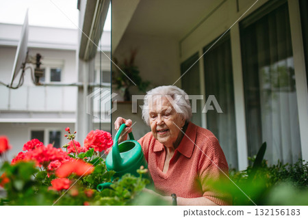 Elderly woman watering potted flowers on balcony. Elderly woman watering potted flowers on balcony. 132156183