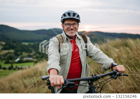 Smiling senior man cycling in nature at sunset. 132156246