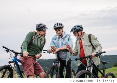 Grandfather, father and teen boy on cycling trip looking at map in smartphone. Grandfather, father and teen boy on cycling trip looking at map in smartphone. 132156253