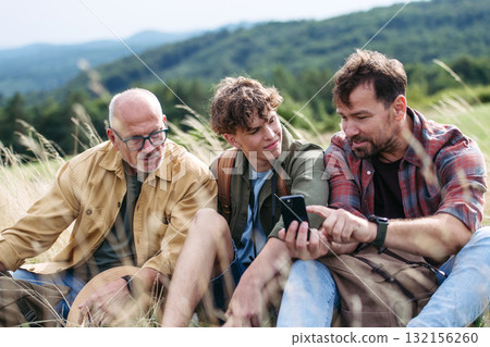 Grandfather, father and teen boy hiking togeter in nature, resting on meadow. 132156260