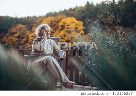 Portrait of smiling elderly lady relaxing on terrace during warm autumn day. Portrait of smiling elderly lady relaxing on terrace during warm autumn day. 132156287