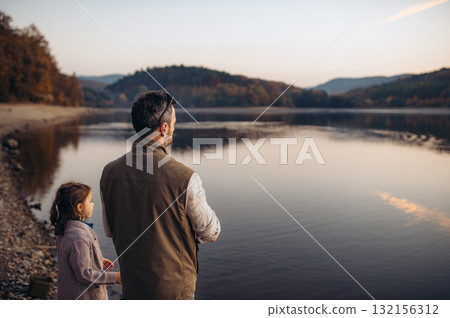 Dad and daughter looking at lake during warm autumn evening. 132156312