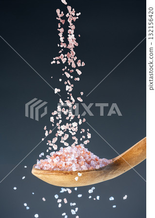 Heap of rose-colored sea salt fall from above onto a wooden spoon, great for kitchen and mineral nutrition images. Heap of rose-colored sea salt fall from above onto a wooden spoon, great for kitchen and mineral nutrition images. 132156420