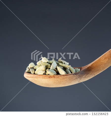 Whole cardamom seeds in natural wood spoon, ideal for aromatic seasoning and exotic recipe preparation concepts 132156423