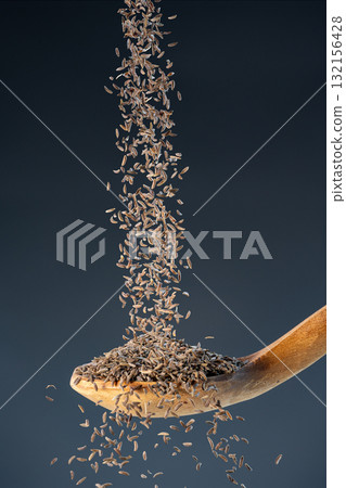 Brown cumin seeds fall from above onto a wooden spoon, ideal for aromatic seasoning and exotic recipe preparation concepts. Brown cumin seeds fall from above onto a wooden spoon, ideal for aromatic seasoning and exotic recipe preparation concepts. 132156428