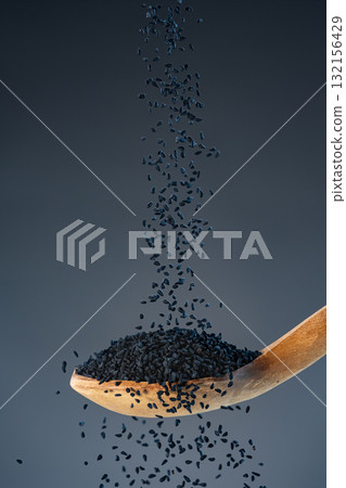 Black nigella seeds fall from above onto a wooden spoon, ideal for spice, seasoning and exotic recipe preparation concepts. Black nigella seeds fall from above onto a wooden spoon, ideal for spice, seasoning and exotic recipe preparation concepts. 132156429