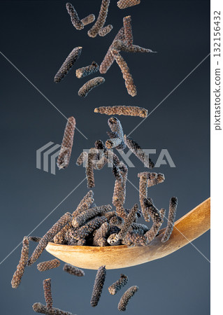 Traditional long pepper spice (Piper longum) fall from above onto a wooden spoon against neutral background for culinary concept. Traditional long pepper spice (Piper longum) fall from above onto a wooden spoon against neutral background for culinary concept. 132156432