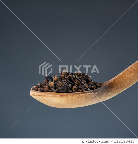 Whole dried cloves arranged on natural wooden spoon against neutral background, perfect for culinary and cooking themes Whole dried cloves arranged on natural wooden spoon against neutral background, perfect for culinary and cooking themes 132156435