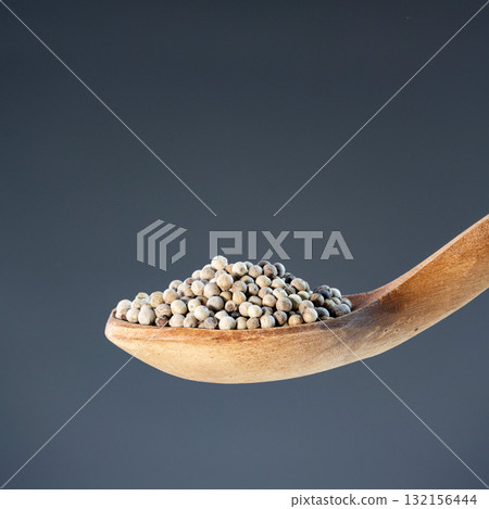 Whole white peppercorns displayed on natural wooden spoon against neutral background for culinary and cooking themes Whole white peppercorns displayed on natural wooden spoon against neutral background for culinary and cooking themes 132156444