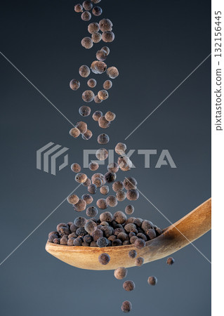 Close-up of dried pimento corns fall from above onto a wooden spoon, perfect for gourmet food photography and spice concepts. Close-up of dried pimento corns fall from above onto a wooden spoon, perfect for gourmet food photography and spice concepts. 132156445