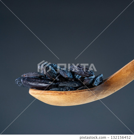 Close-up of black aromatic beans on carved wooden utensil, showcasing premium culinary ingredients and natural textures Close-up of black aromatic beans on carved wooden utensil, showcasing premium culinary ingredients and natural textures 132156452
