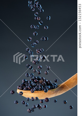 Fresh dried juniper fall from above onto a wooden spoon, ideal for culinary herbs and aromatic cooking ingredient concepts 132156453