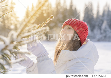 Woman inspecting snow-covered pine tree in winter landscape during sunny afternoon Woman inspecting snow-covered pine tree in winter landscape during sunny afternoon 132156610