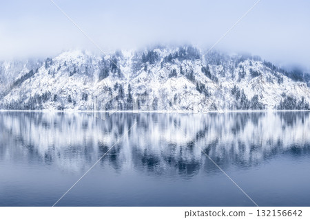 A tranquil winter landscape with snowcovered mountains and serene water reflections A tranquil winter landscape with snowcovered mountains and serene water reflections 132156642