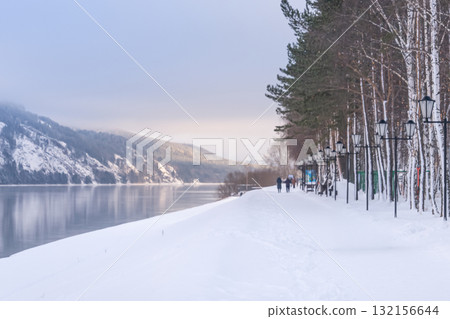 Divnogorsk city embankment in winter. A path along the river and winter mountains in the suburbs of Krasnoyarsk, a cozy riverbank in Russia. Experience the beauty of a Winter Wonderland with a serene 132156644