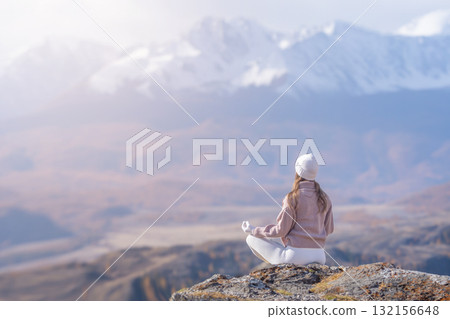 On a serene morning, a woman sits in meditation on a mountain ledge, surrounded by autumn colors and majestic peaks, embracing tranquility and nature's beauty. On a serene morning, a woman sits in meditation on a mountain ledge, surrounded by autumn colors and majestic peaks, embracing tranquility and nature's beauty. 132156648