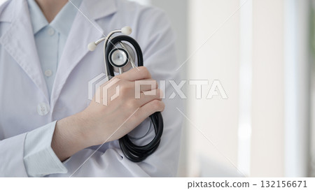 Close up of a doctor hand holding a stethoscope while standing with arms crossed in diagnosis room. 132156671