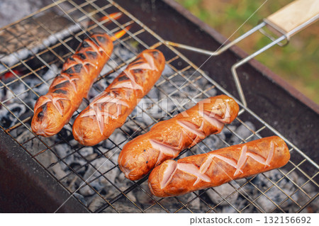 Juicy grilled sausages sizzling on a backyard grill during an autumn picnic in nature close up Juicy grilled sausages sizzling on a backyard grill during an autumn picnic in nature close up 132156692