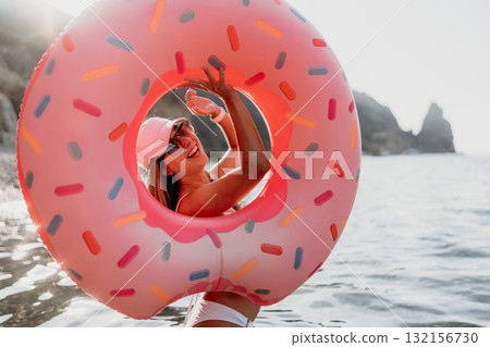 Woman, donut, ocean. Happy woman playing with a large pink donut ring in the ocean during summer vacation. Woman, donut, ocean. Happy woman playing with a large pink donut ring in the ocean during summer vacation. 132156730