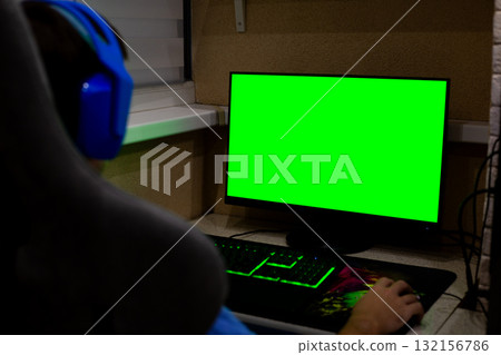 Person sits at gaming desk with green screen displayed on monitor. The setup invites creative integration, allowing users to place their own projects in gaming environment 132156786