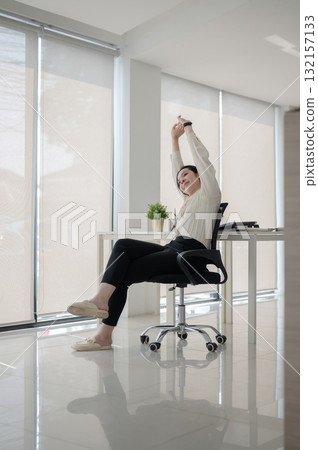 Female office worker or businesswoman sitting with both arm raised on swivel chair in empty office. Female office worker or businesswoman sitting with both arm raised on swivel chair in empty office. 132157133