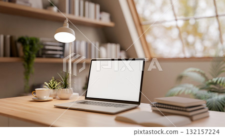 White screen laptop with coffee cup and books on wooden table in the bright room under roof window 132157224