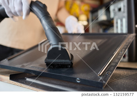 A man cleans a computer case with a vacuum in a bright room, stressing workspace tidiness 132159577