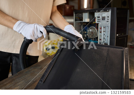 A man cleans a computer case with a vacuum in a bright room, stressing workspace tidiness A man cleans a computer case with a vacuum in a bright room, stressing workspace tidiness 132159583