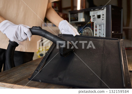 A man cleans a computer case with a vacuum in a bright room, stressing workspace tidiness A man cleans a computer case with a vacuum in a bright room, stressing workspace tidiness 132159584