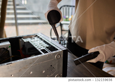 A man cleans a computer case with a vacuum in a bright room, stressing workspace tidiness A man cleans a computer case with a vacuum in a bright room, stressing workspace tidiness 132159656