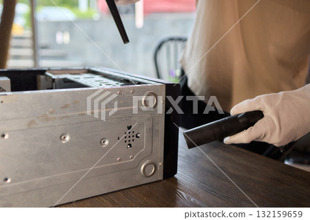 A man cleans a computer case with a vacuum in a bright room, stressing workspace tidiness 132159659