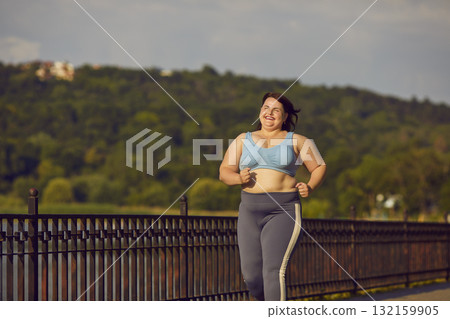 Happy, smiling, overweight woman in sportswear jogging on a city bridge in summer Happy, smiling, overweight woman in sportswear jogging on a city bridge in summer 132159905